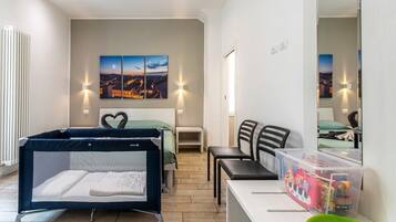 A bedroom with a bed, a desk, a chair, a crib, and a wall-mounted TV.