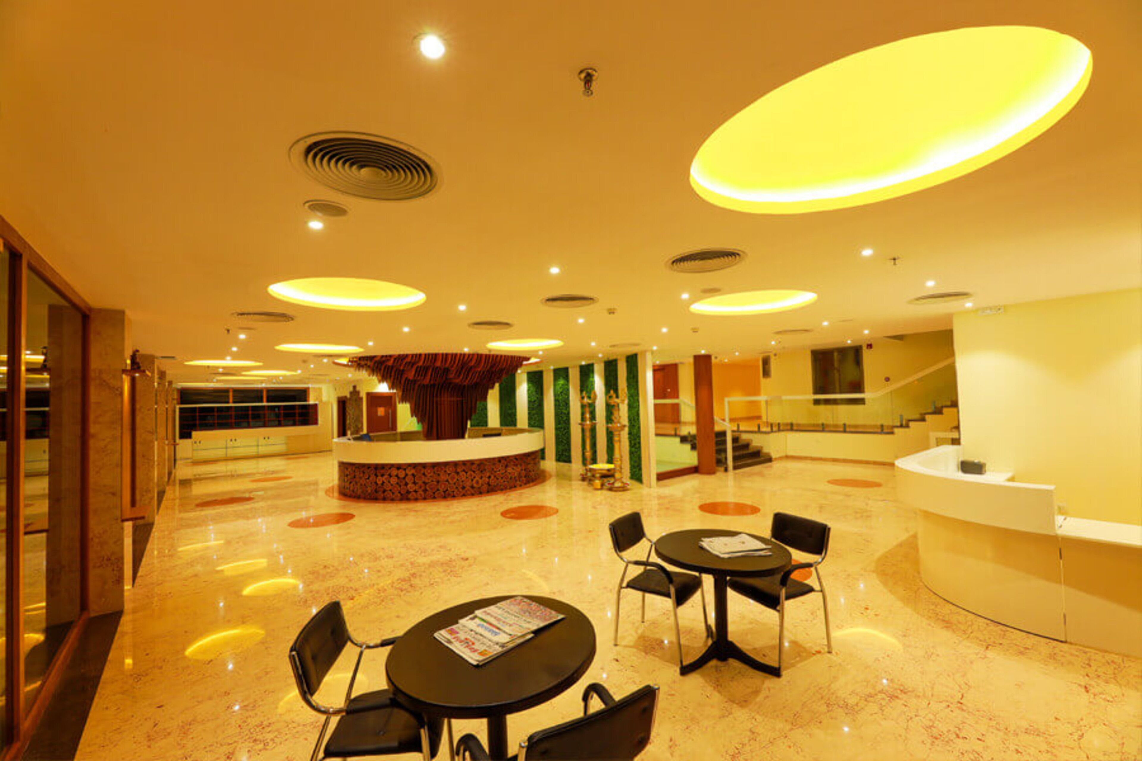 A spacious lobby with a central reception desk, multiple seating areas, and a staircase leading to upper floors.