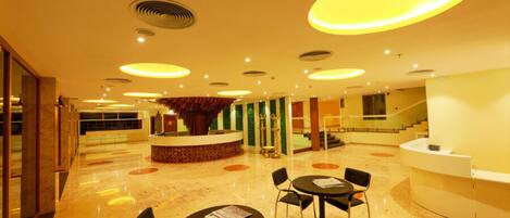 A spacious lobby with a central reception desk, multiple seating areas, and a staircase leading to upper floors.