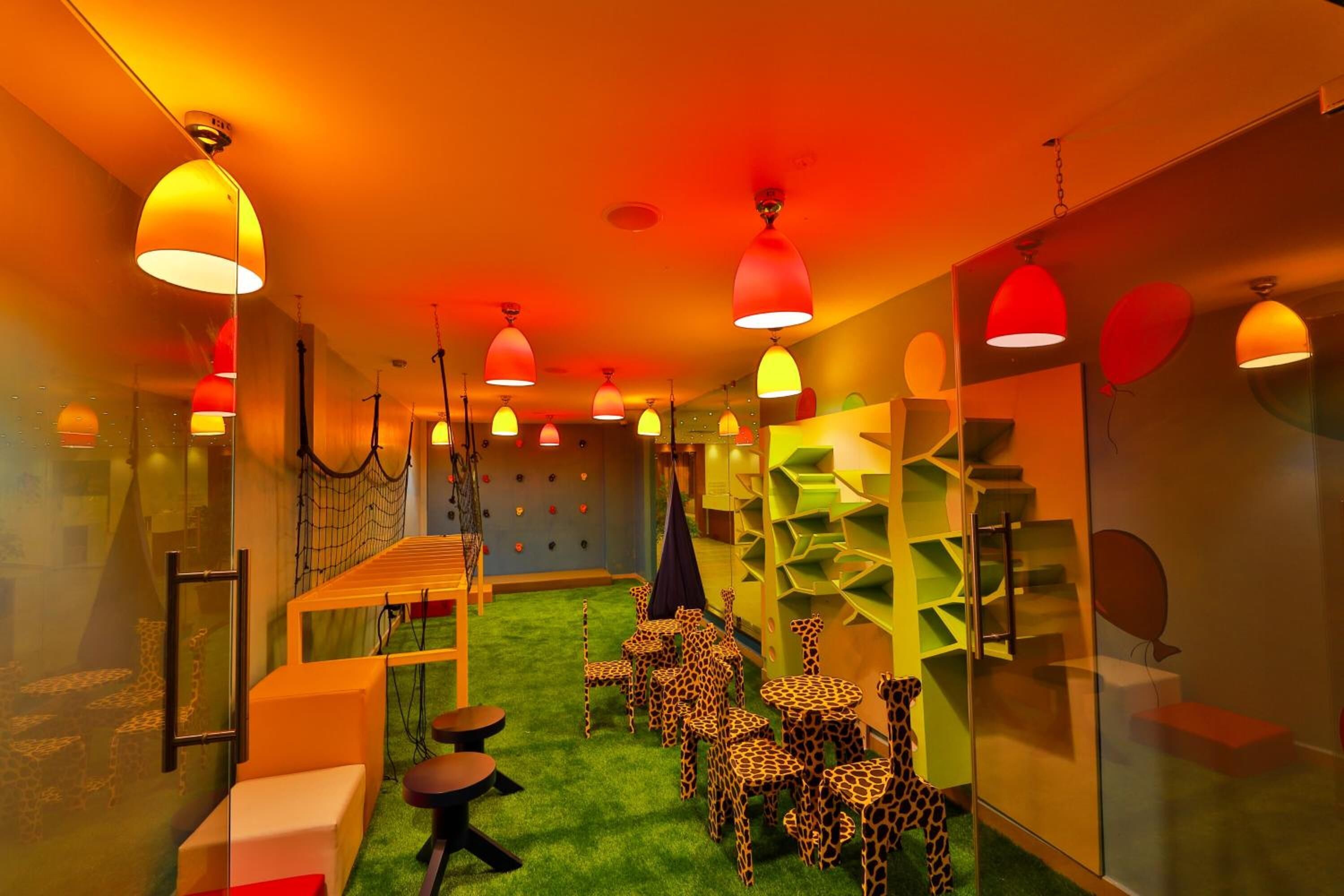 A room with a green carpet, giraffe-themed chairs, and red pendant lights.