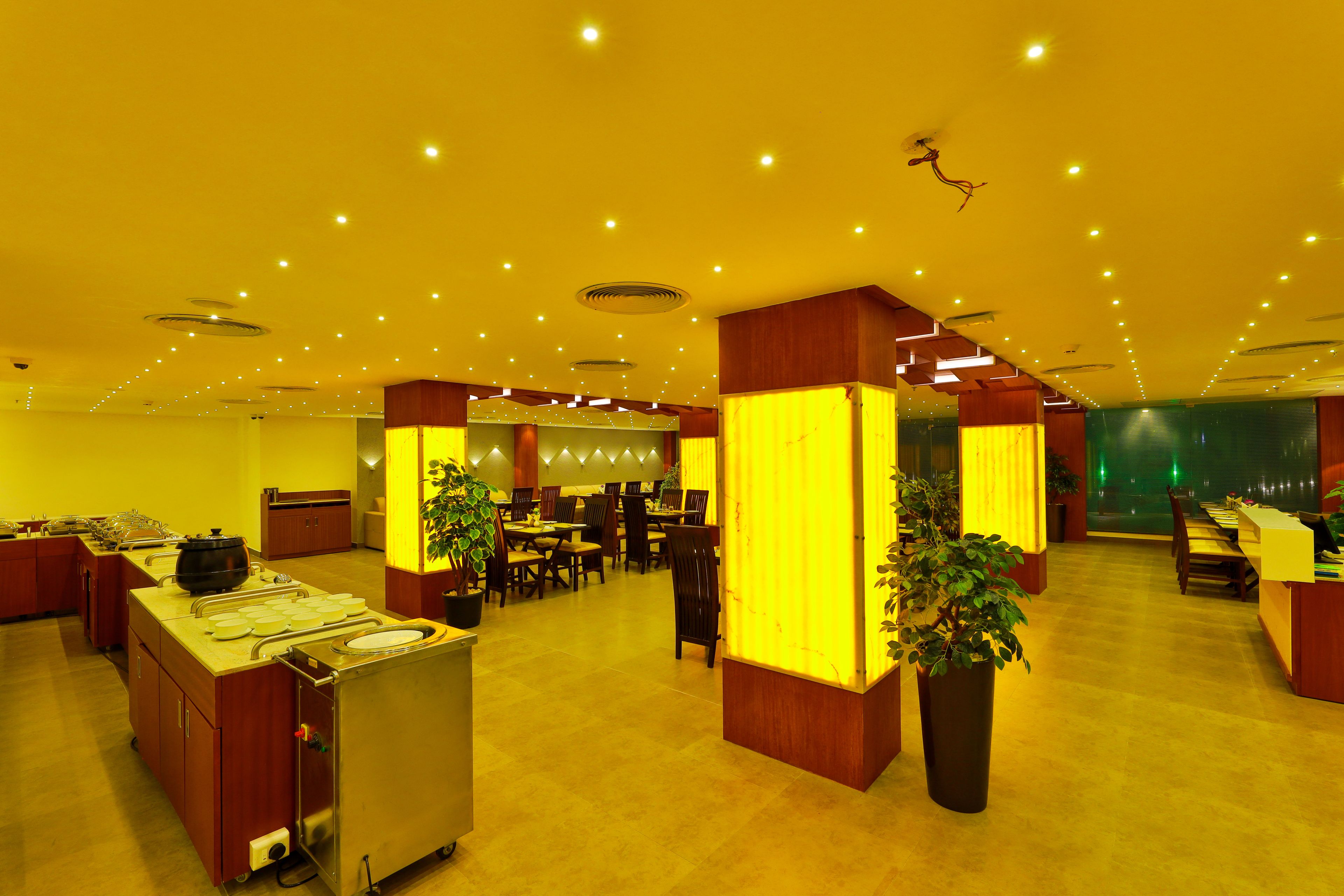 Un hall d’hôtel doté d’un comptoir d’accueil central, de plusieurs tables et de plantes en pot.