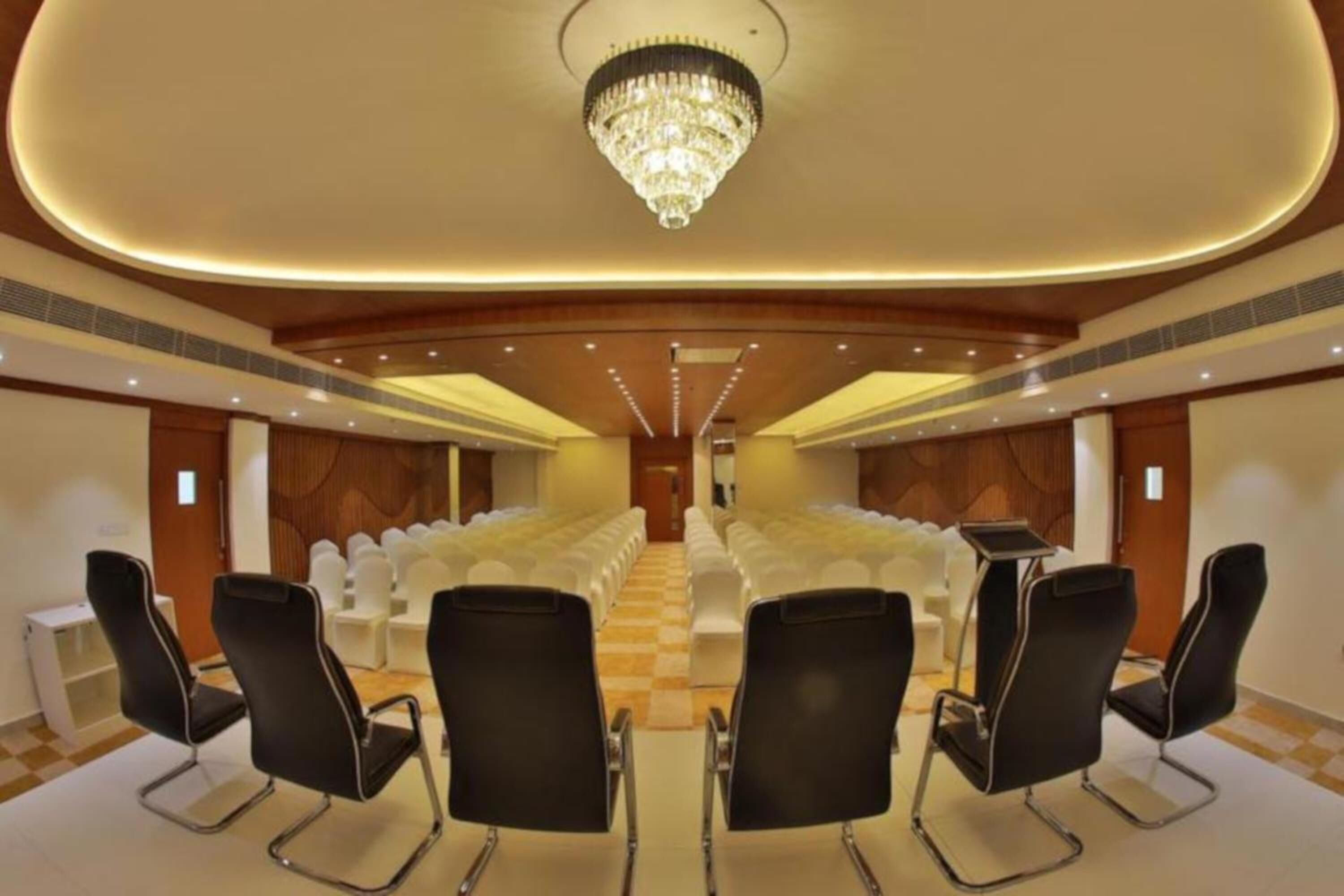A conference room with rows of white chairs, a chandelier, and a checkered floor.