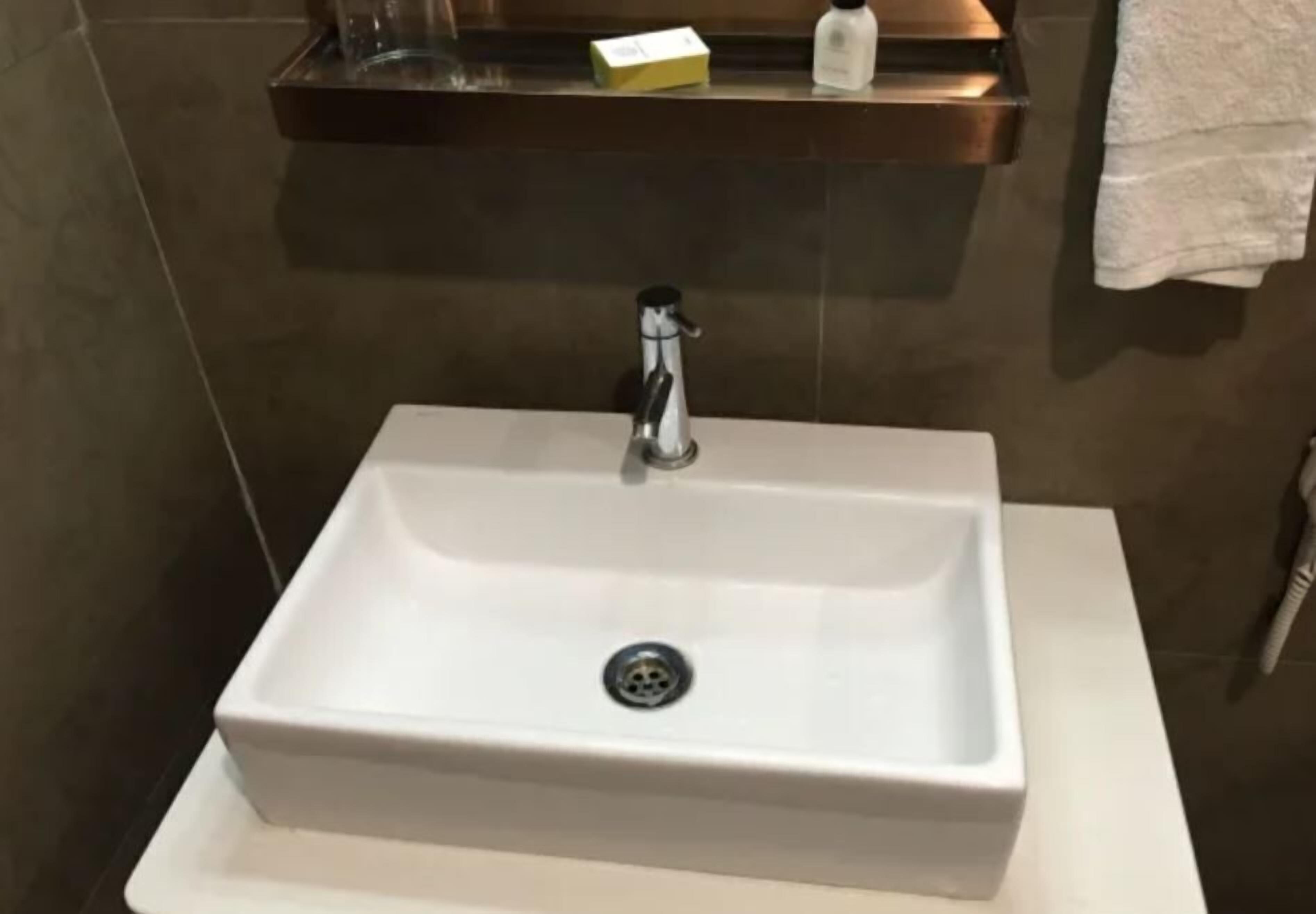 A bathroom with a white sink, a faucet, and a shelf above the sink holding a soap dispenser and a small box.