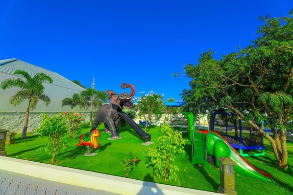 Un parque infantil con tobogán, columpios y una gran estatua de elefante.