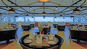 A spacious outdoor dining area with multiple tables and chairs, large hanging pendant lights, and a view of the sky through the roof structure. - Annai Resorts & Spa (Nagercoil)