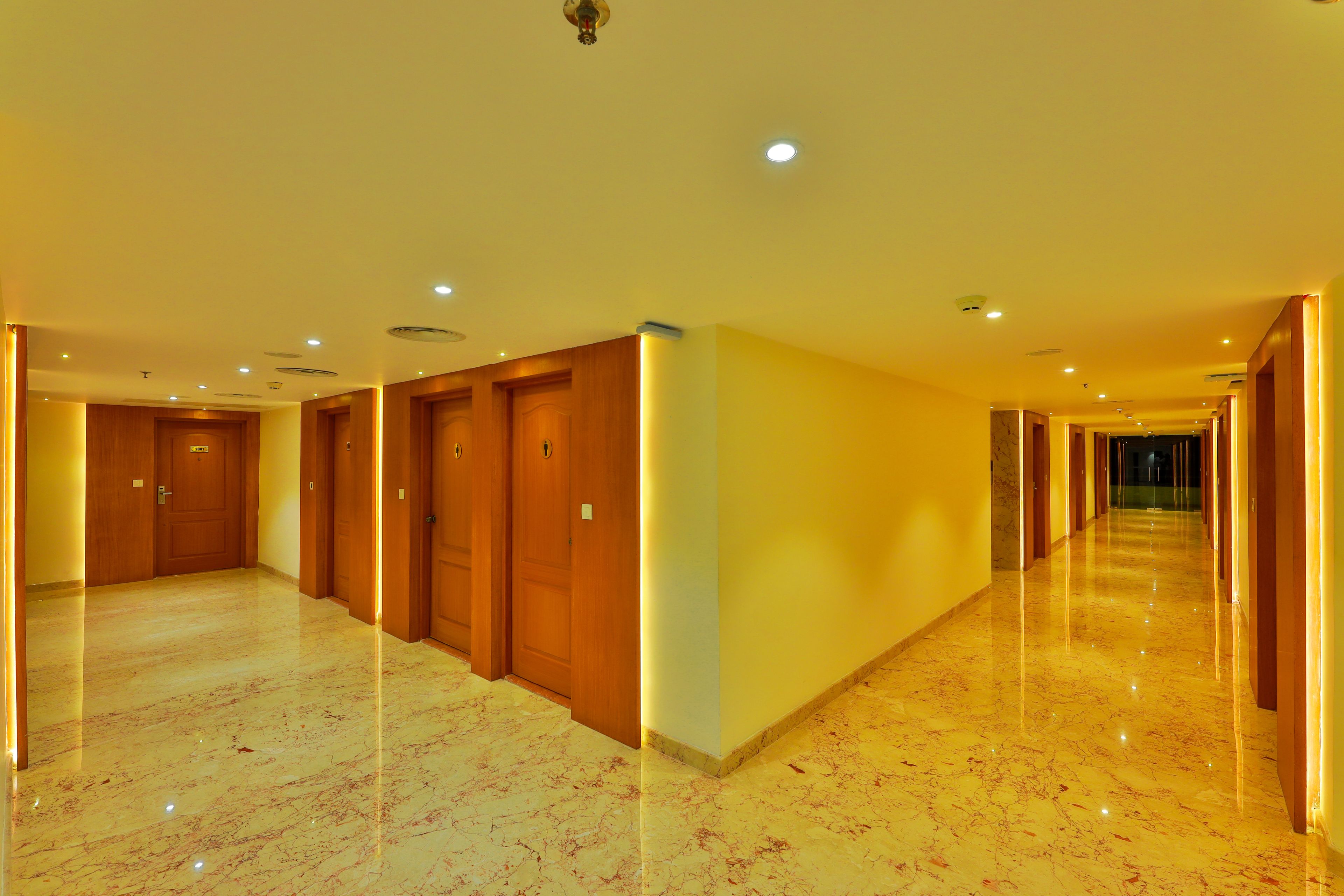 A hotel corridor with wooden doors, marble floors, and recessed lighting.