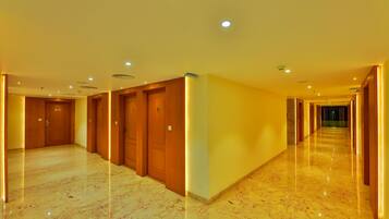 A hotel corridor with wooden doors, marble floors, and recessed lighting.