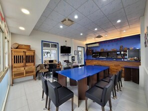 A room with a blue table, black chairs, a wooden cabinet, and a counter with various items.
