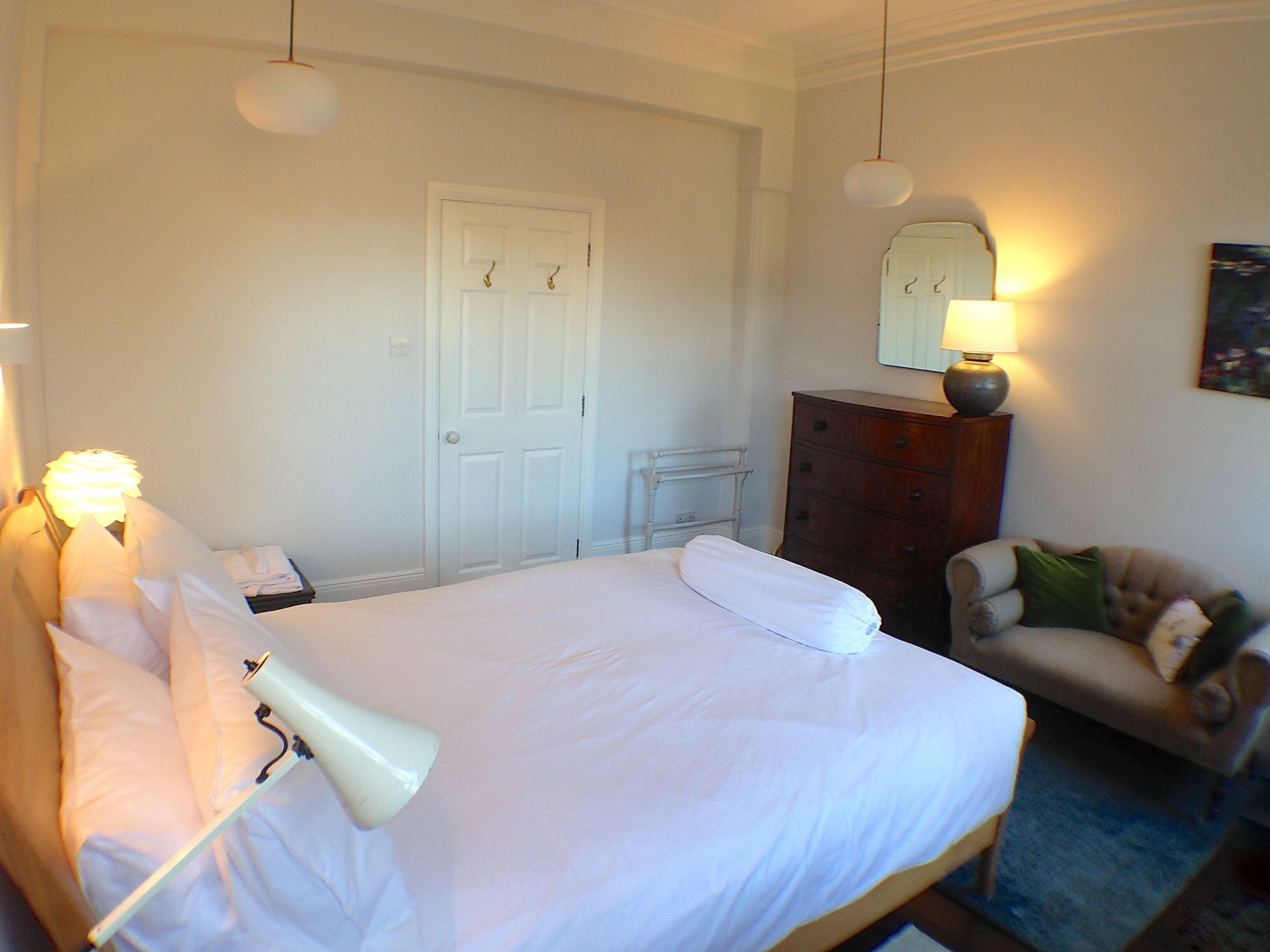A hotel room with a bed, bedside lamps, a dresser, a chair, and a mirror on the wall.