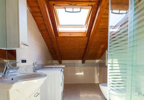 Casa de banho com claraboia, lavatório, máquina de lavar roupa e sanita.