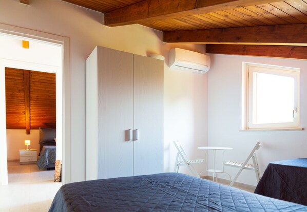 Un dormitorio con cama, armario, una mesita y una ventana.