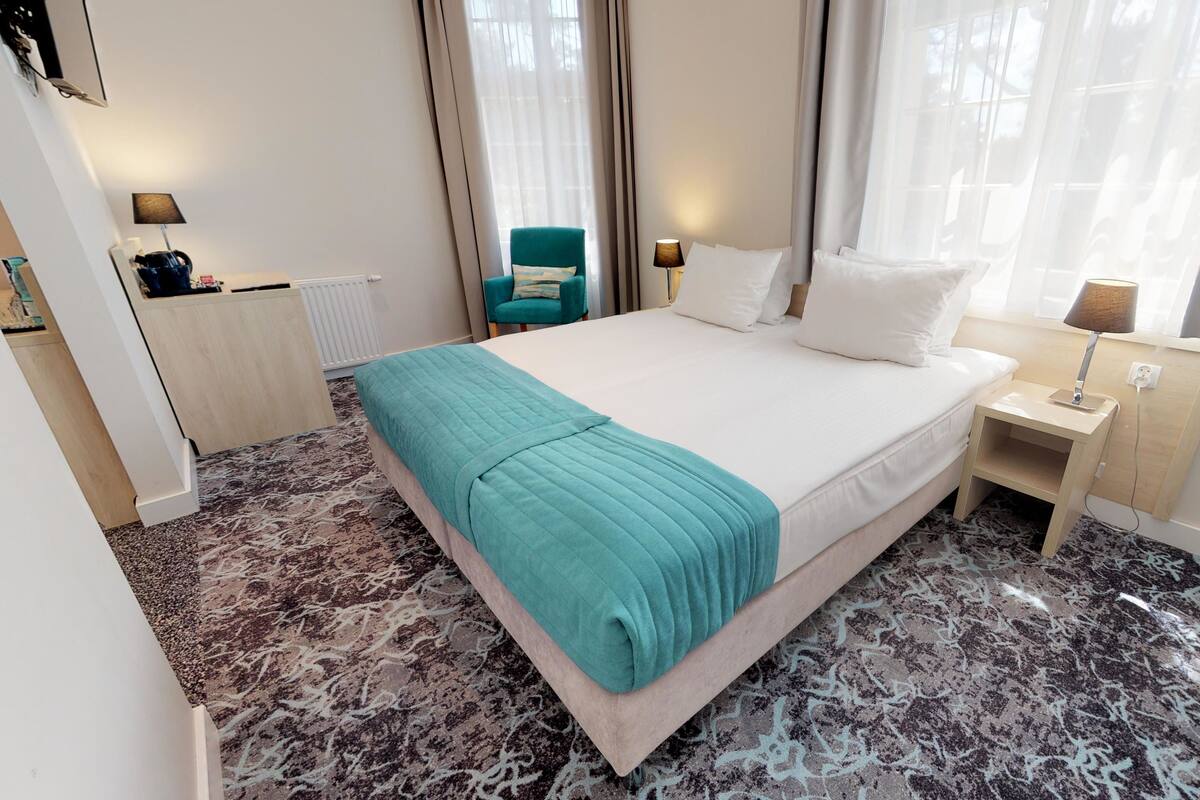 A hotel room with a bed, a nightstand, a lamp, a chair, and a radiator.