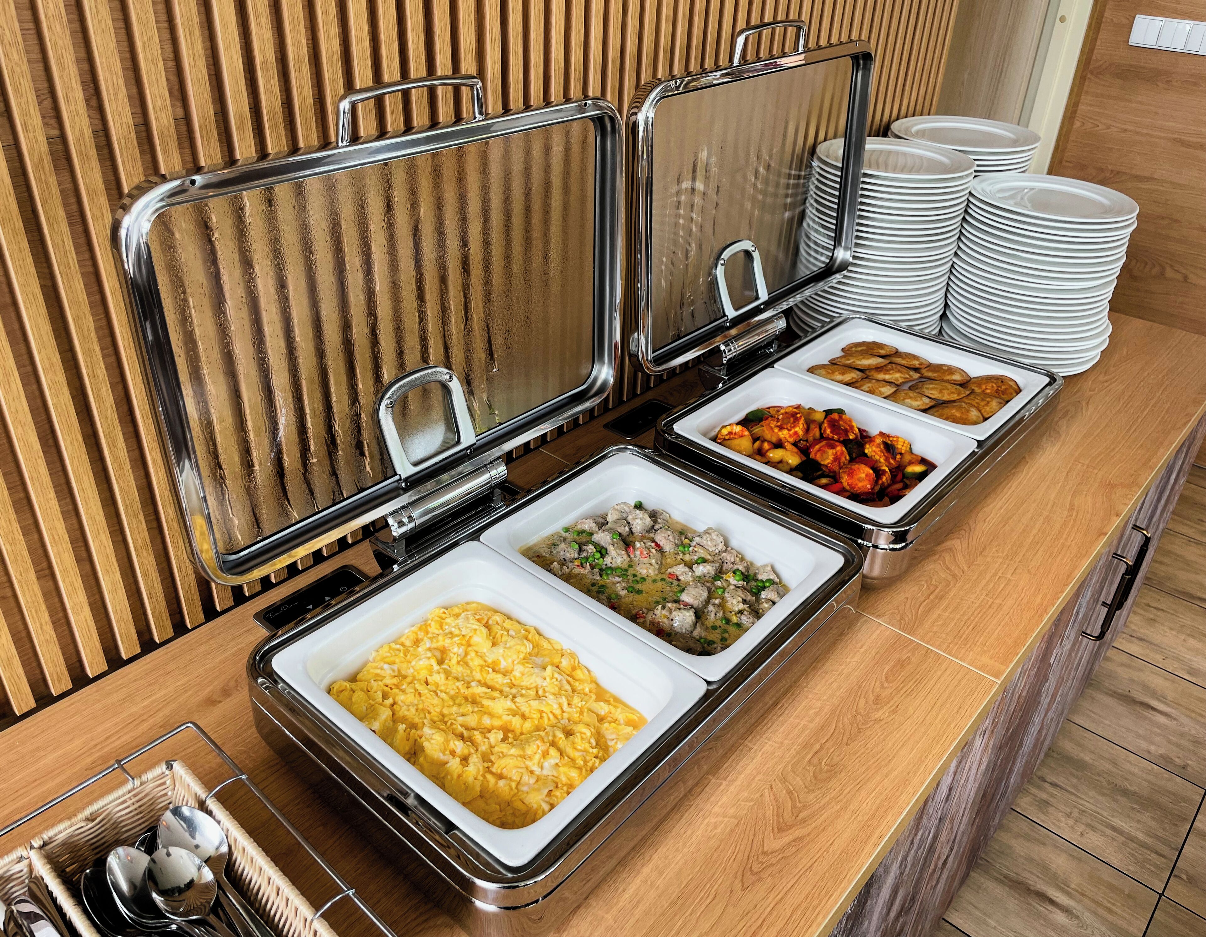 Montaje de bufé con múltiples bandejas de comida, incluyendo huevos revueltos, albóndigas y verduras.