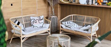 A cozy room with two wicker sofas, a round ottoman, and a wooden reception desk with a vase of pampas grass.