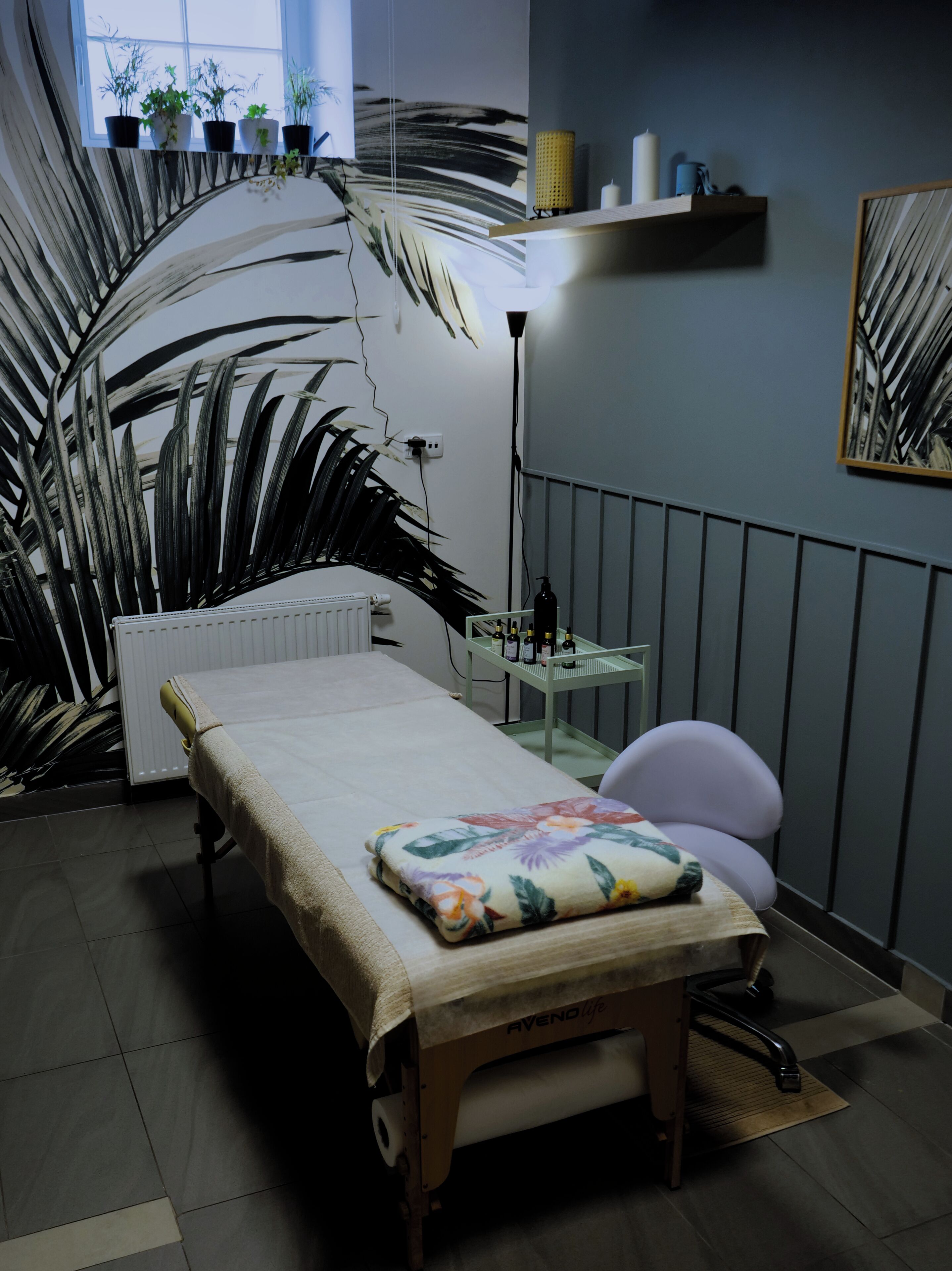 A treatment room with a bed, a chair, a small table with bottles, and a shelf with candles.