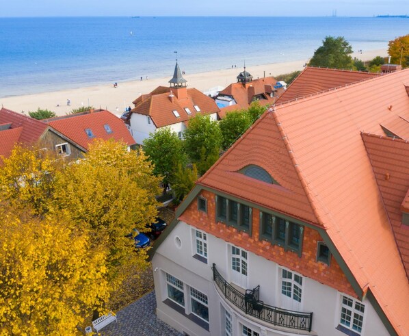 A coastal town with red-roofed buildings, a beach, and autumn foliage.
