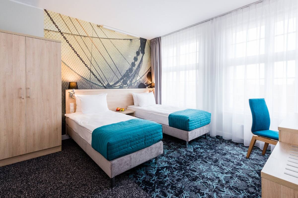 A hotel room with two beds, a large wardrobe, a desk, and a chair.