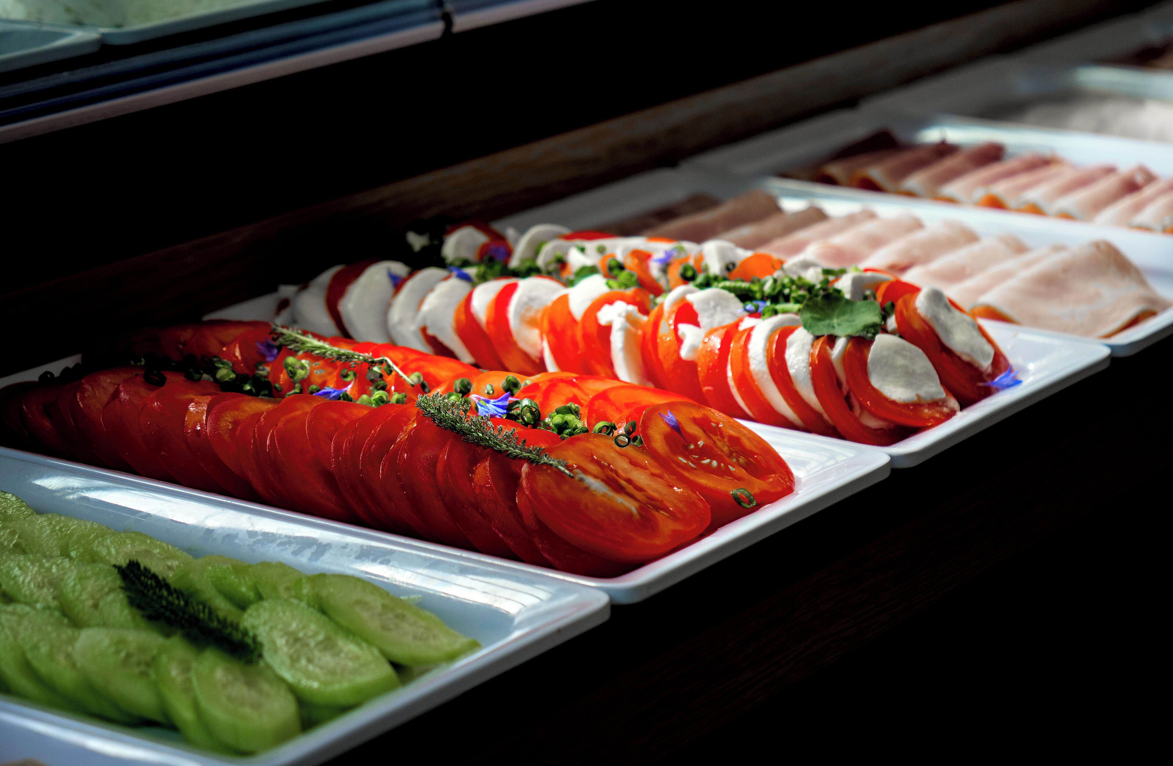 En buffet med forskellige retter, blandt andet skiverede tomater, agurker og andre grøntsager.