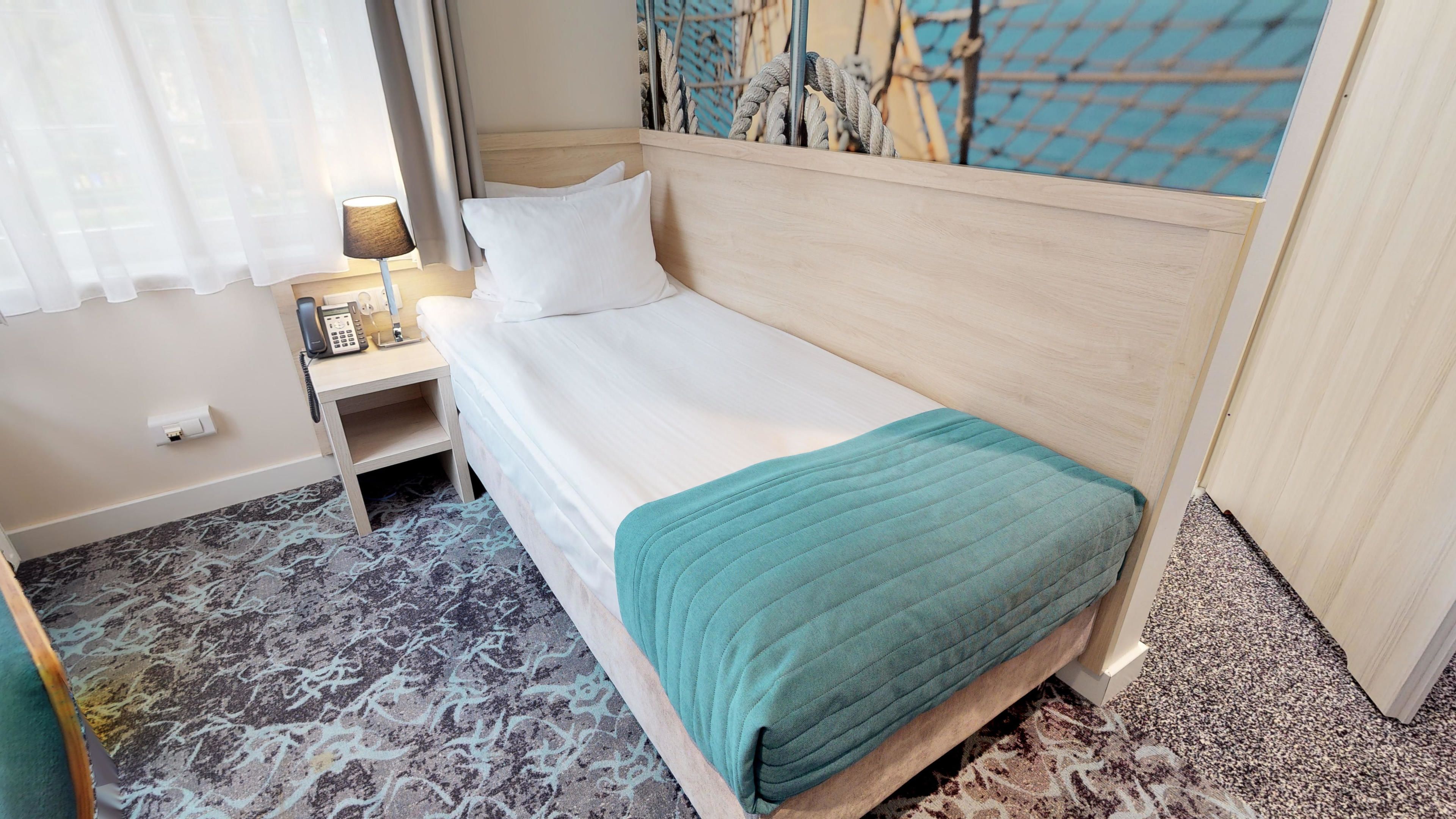 A single bed with a wooden headboard, a bedside table with a lamp, and a patterned carpet.
