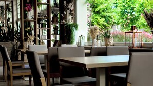 Un restaurante con mesas y sillas de madera, rodeado de estanterías con plantas y flores.