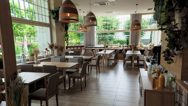 Un restaurante espacioso con amplias ventanas, mesas de madera y lámparas colgantes.