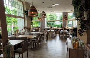 A spacious restaurant with large windows, wooden tables, and hanging pendant lights. - Hotel Eureka (Sopot)