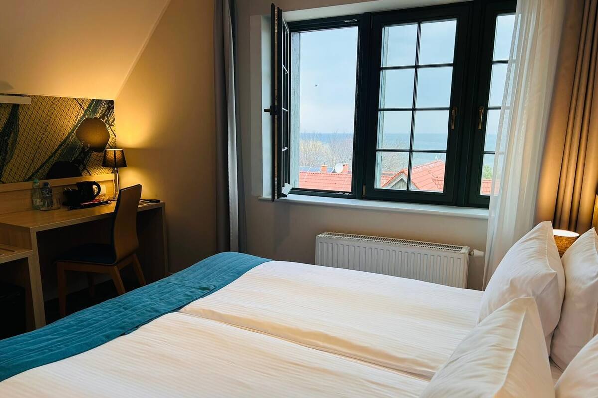 A hotel room with a bed, a desk, a chair, a window with a view, and a radiator.