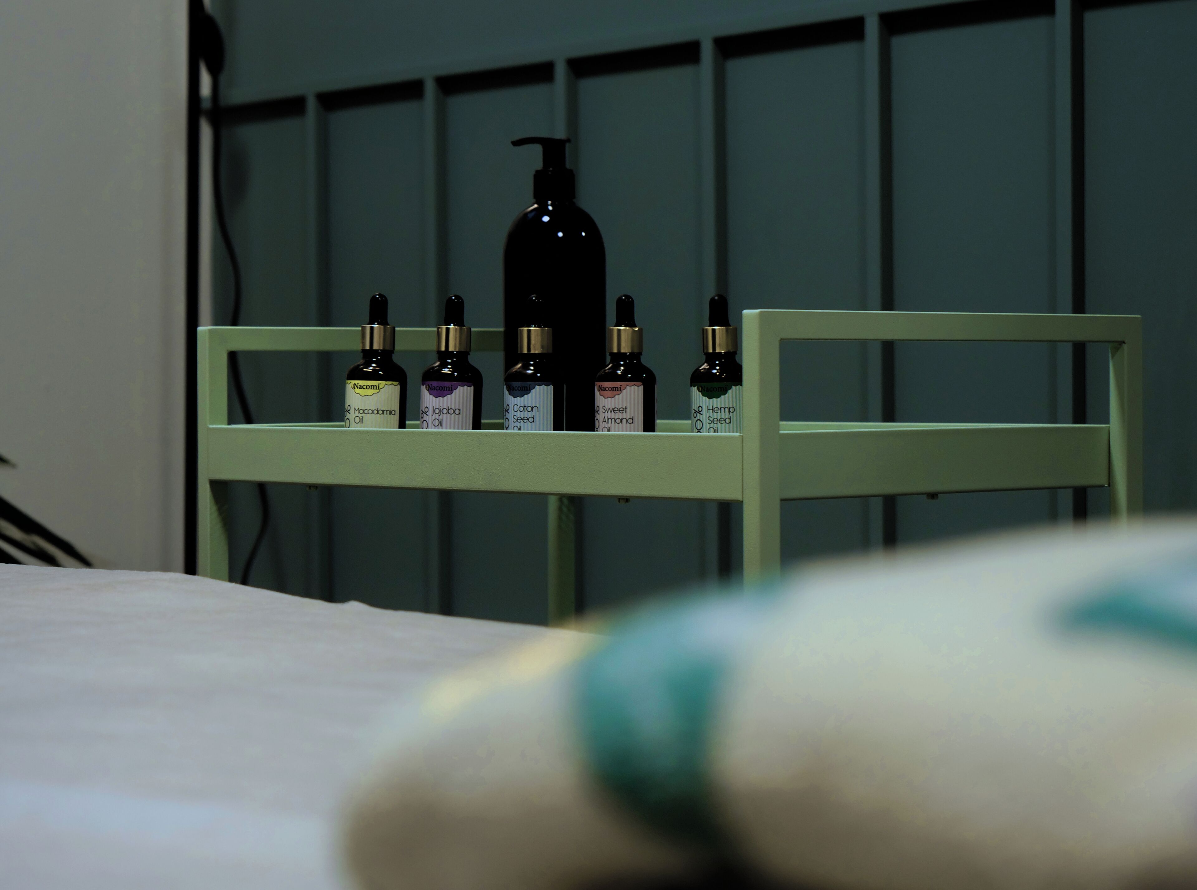 A bed with a white sheet and a green headboard. On the headboard, there are six bottles of various essential oils.