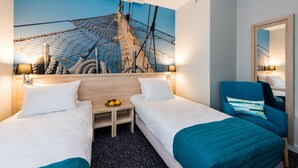 Habitación de hotel con dos camas, una mesita con fruta, una silla y un gran mural en la pared con aparejo de barco.