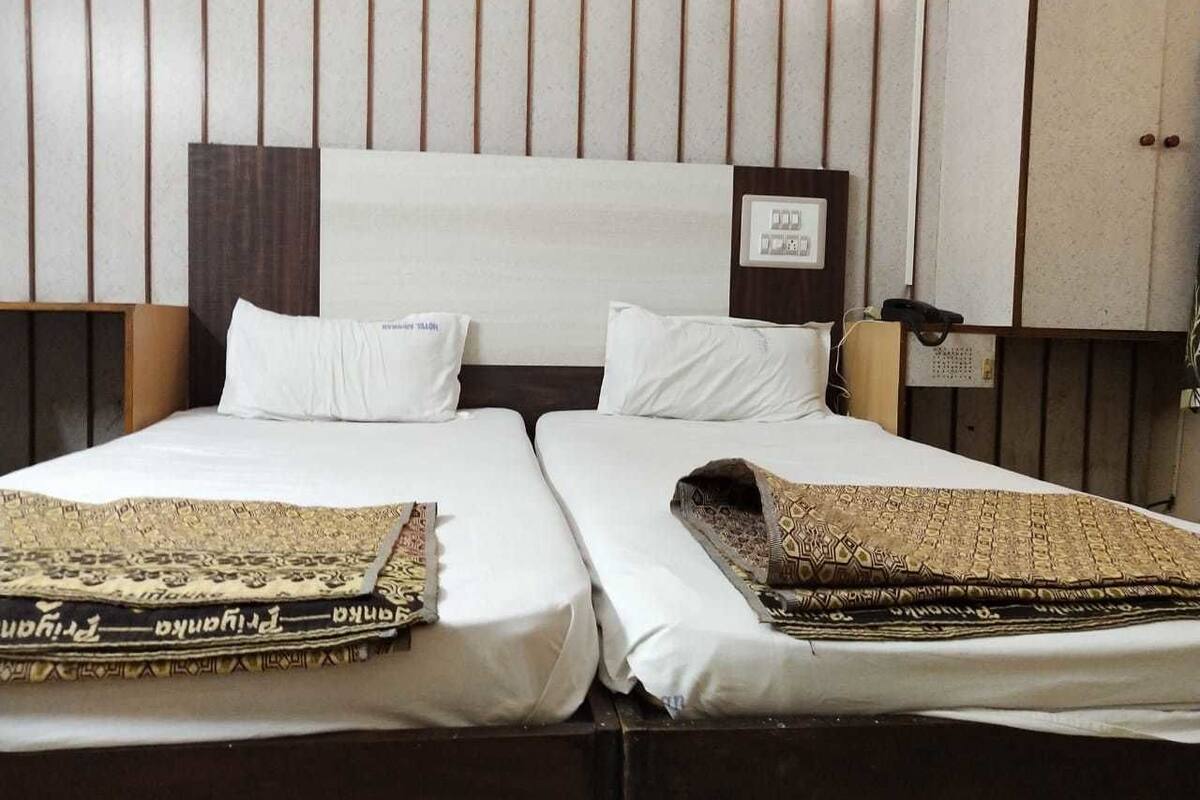 Cama doble con sábanas blancas y una colcha estampada, mesita de noche con lámpara y armario de madera.