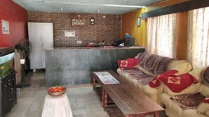 A living room with a sofa, a coffee table, a small table with a bowl, a refrigerator, and a stone-patterned wall.