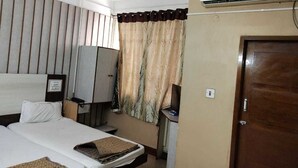 A hotel room with a bed, a desk, a television, and an air conditioning unit.