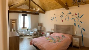 Ein Schlafzimmer mit Holzboden, einem Bett mit floralem Überwurf, einem Schreibtisch mit Stühlen und einer Wandmalerei.