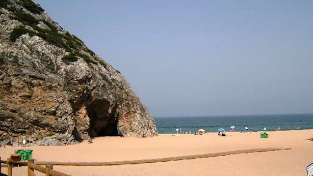 Ein Strand mit einer felsigen Klippe und einer Holzpromenade, die zum Ufer führt.