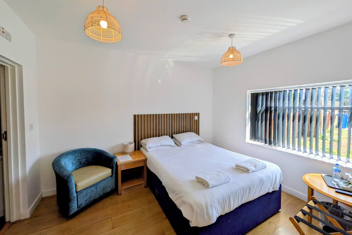 A bedroom with a bed, bedside table, chair, and a window with blinds.
