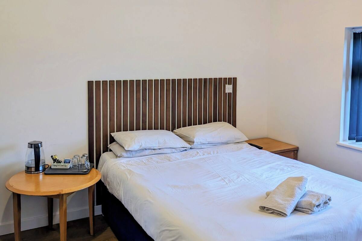 A neatly made bed with white linens, a wooden headboard, and two bedside tables with a kettle and glasses.