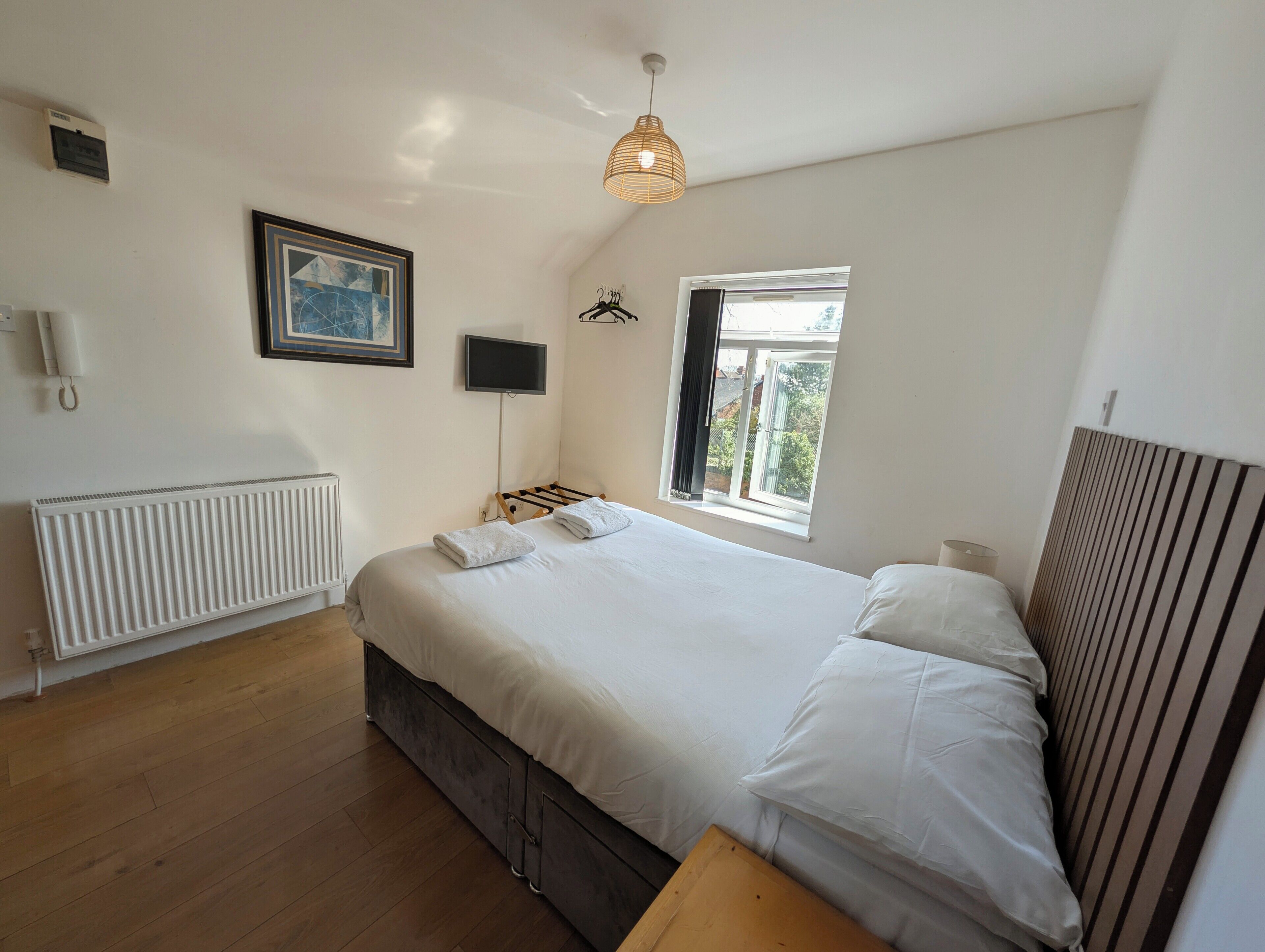 A bedroom with a bed, a window, a radiator, a television, and a wall-mounted light fixture.