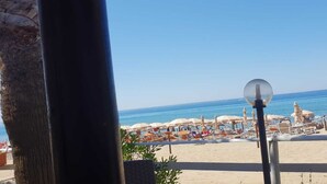 A beach with umbrellas and sun loungers, a clear sky, and the ocean in the background.