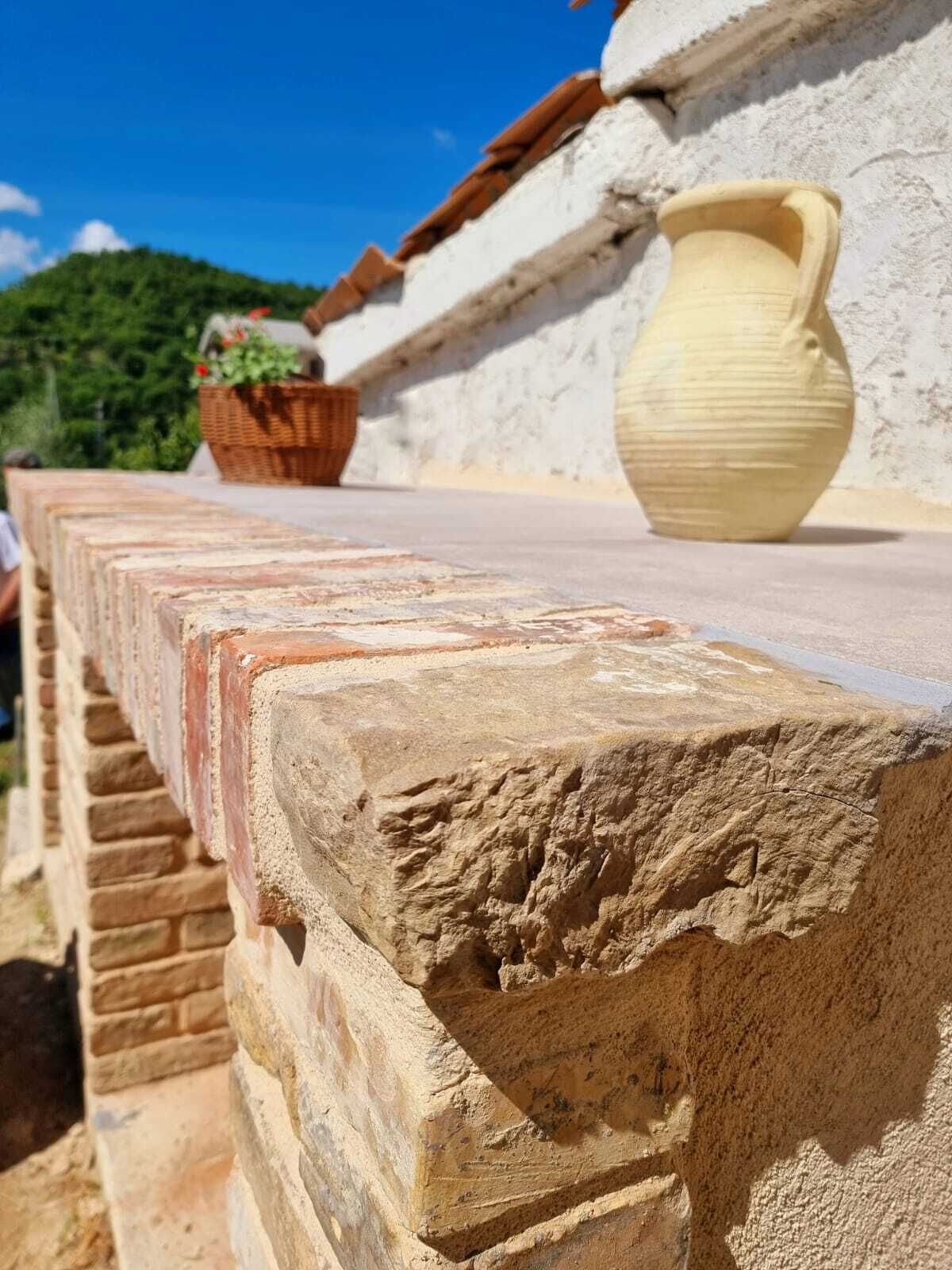 A stone wall with a rough texture and a large, smooth, beige pot on top.
