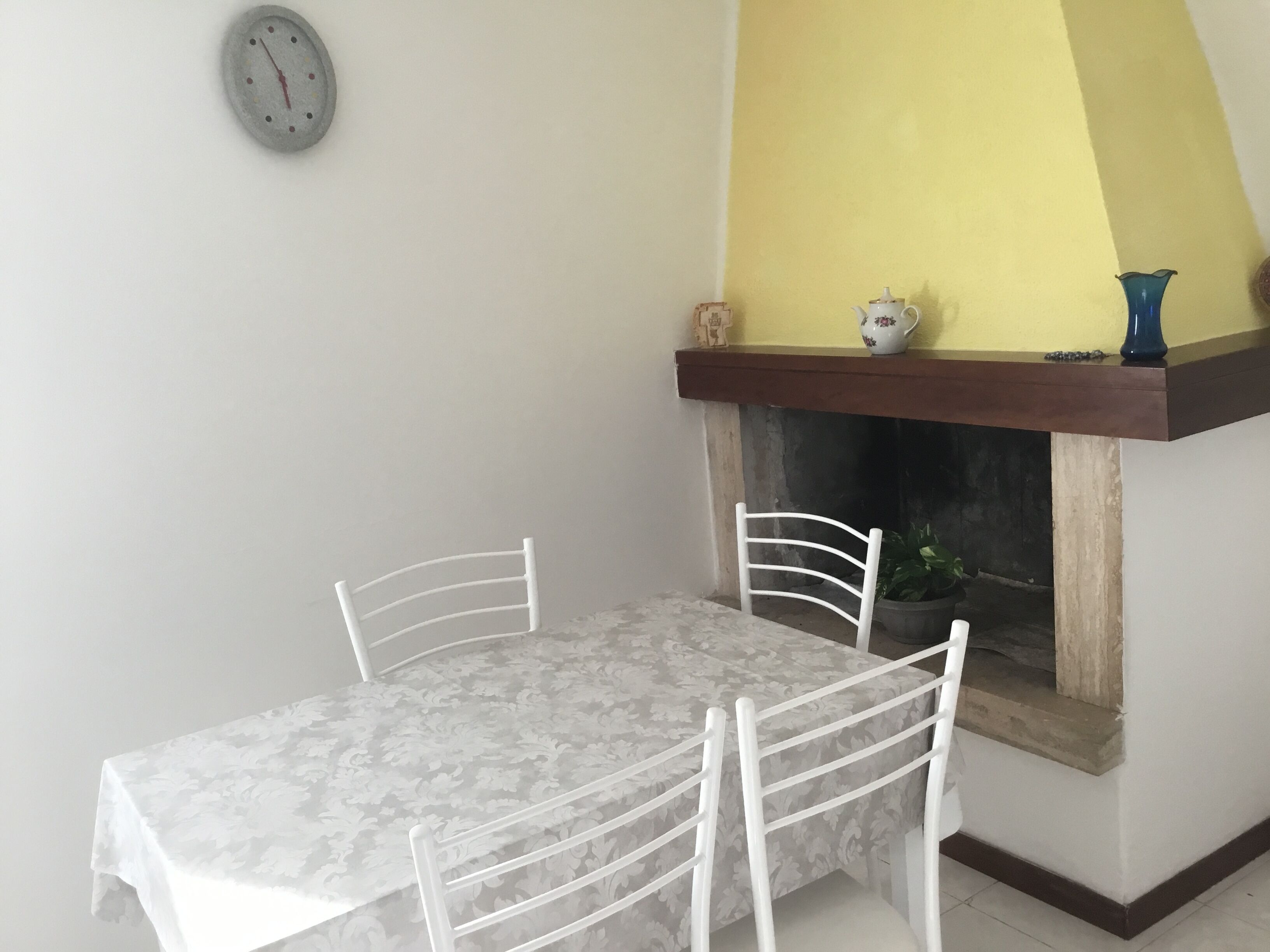 A dining area with a table and chairs, a clock on the wall, and a fireplace with decorative items.