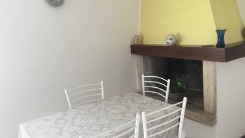 A dining area with a table and chairs, a clock on the wall, and a fireplace with decorative items.