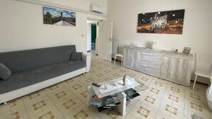A living room with a grey sofa, a glass coffee table with magazines, a white cabinet, and two paintings on the walls. - Vacation House The Laurels (Venarotta)