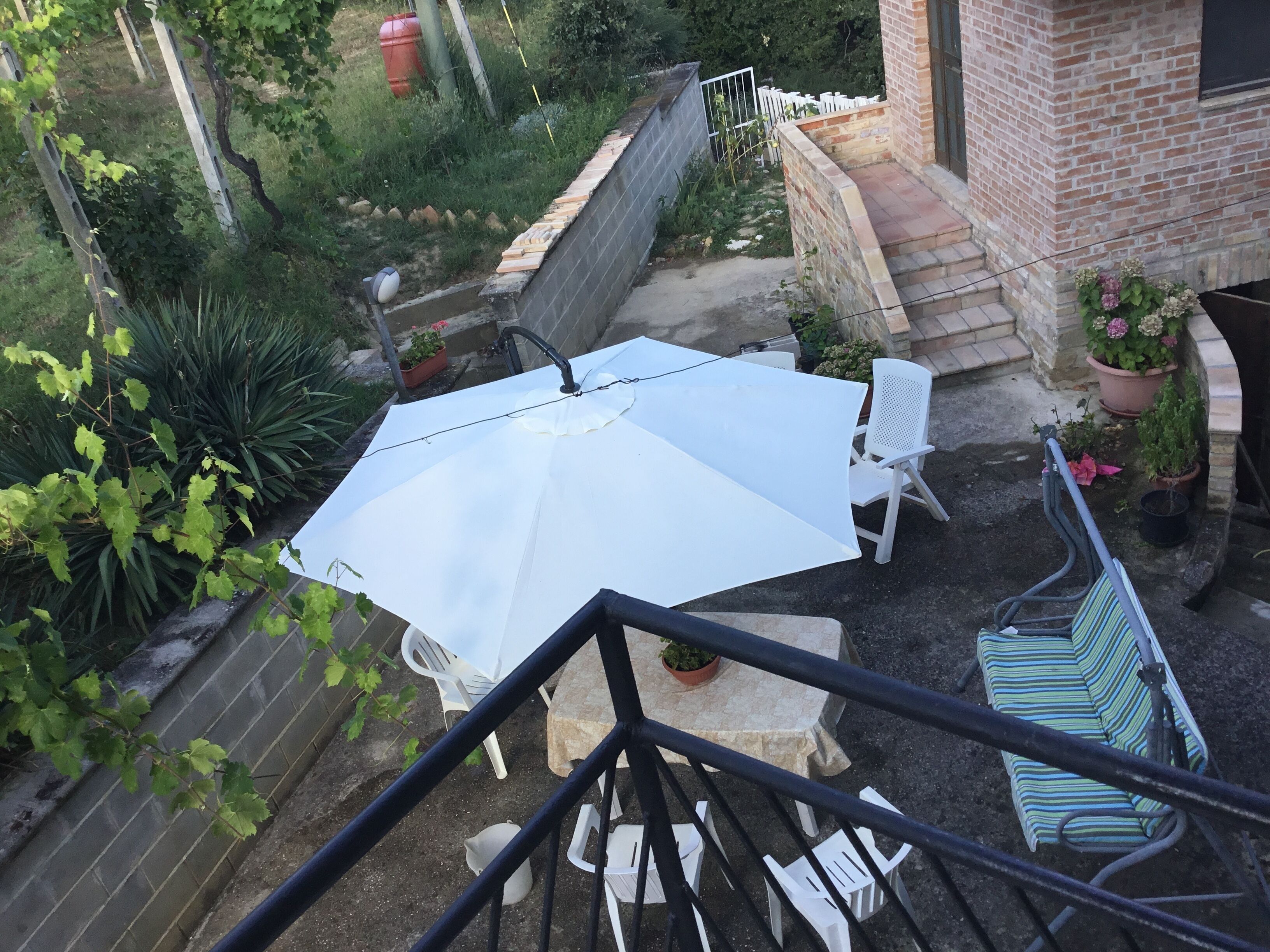 Eine Terrasse mit einem weißen Sonnenschirm, weißen Stühlen und Kübelpflanzen.