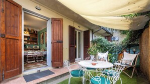 An open patio with a round table and chairs, a wooden door, and a view into the house. - THE HOME OF JASMINE AND MEDLAR, TO MAKE YOU FEEL AT HOME. (Firenze)