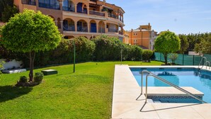 Un área de piscina con una piscina azul cristalina, una pequeña terraza y un césped bien cuidado.