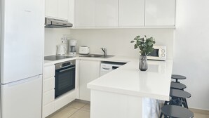 Eine moderne Küche mit weißen Schränken, einem Bosch-Kühlschrank, einer Kaffeemaschine, einer Mikrowelle und einer kleinen Kochinsel mit Sitzgelegenheiten.