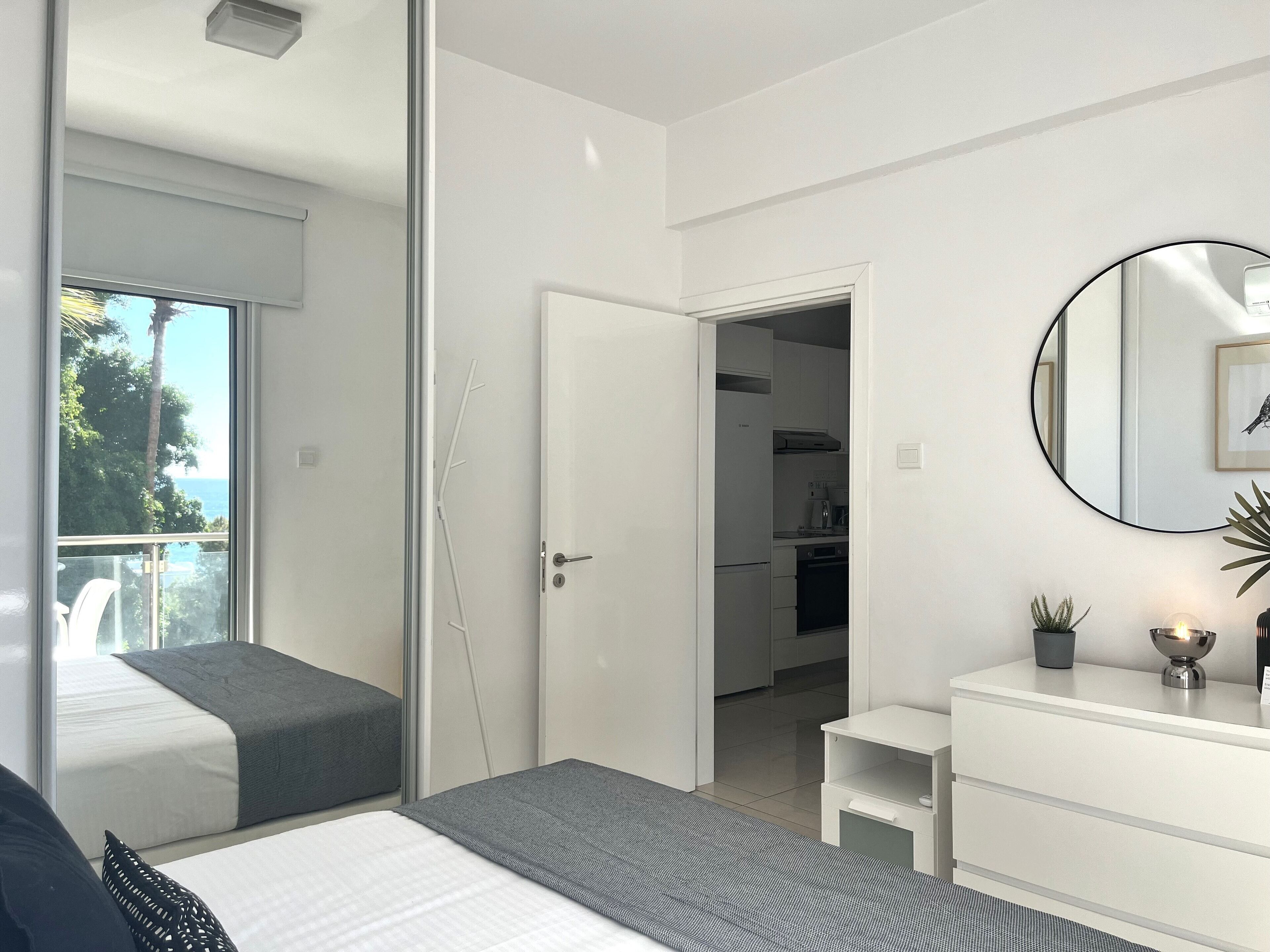 Un dormitorio moderno con cama, mesitas de noche, un pequeño escritorio y vistas a la cocina y al balcón.