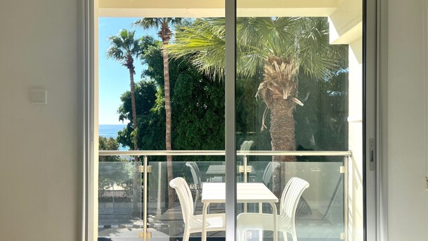 Ein Balkon mit Glastür, weißen Stühlen und einem Tisch.