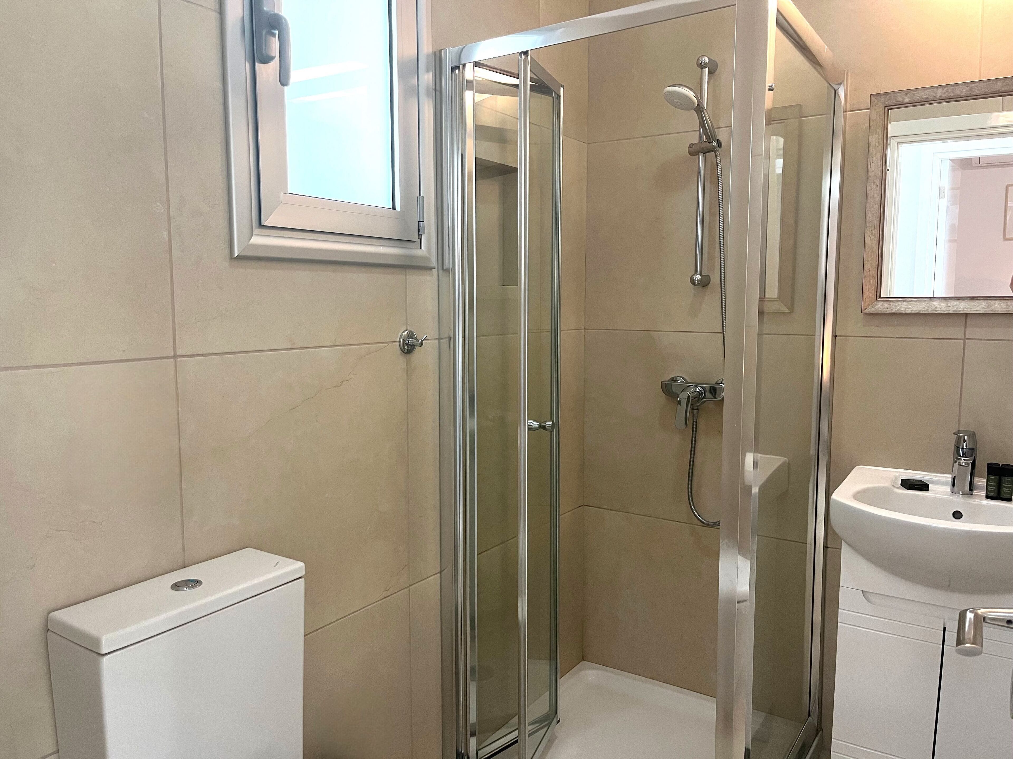 Un baño moderno con ducha de vidrio, lavamanos blanco y retrete.
