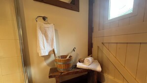 A bathroom with a wooden bench, a wooden bucket, a towel, and a hanging towel.